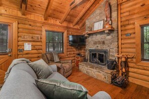 A log cabin interior with a stone fireplace, a television, and a couch.
