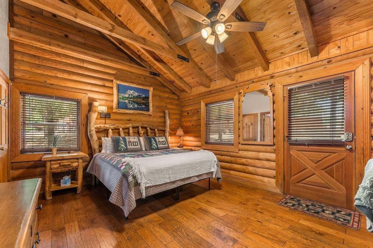 Une chambre dans un chalet en rondins, avec un lit, une table de chevet, un ventilateur de plafond et des murs en bois.
