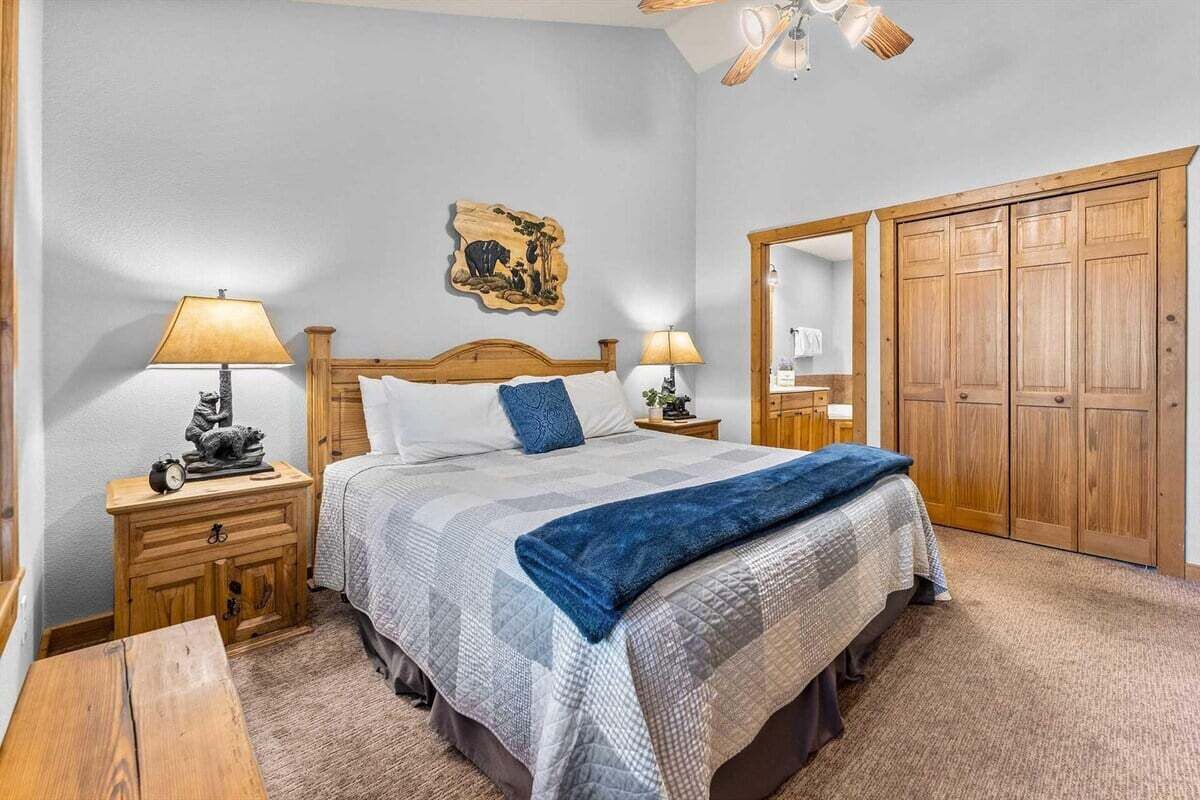 Un dormitorio con cama, dos mesitas de noche, un armario de madera, un ventilador de techo y una obra de arte colgada en la pared.