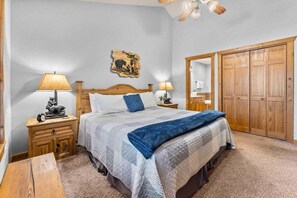 Ein Schlafzimmer mit einem Bett, zwei Nachttischen, einem Holzschrank, einem Deckenventilator und einem an der Wand hängenden Kunstwerk.