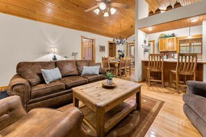 A living room with a brown leather sofa, wooden coffee table, and a dining area with wooden chairs and a table. - StoneBridge Gated Resort-"Four Acorns Lodge"- Free Daily Attraction Tickets (Branson West)