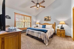 A bedroom with a bed, two bedside lamps, a wooden headboard, a ceiling fan, a window with blinds, and a desk with a lamp and a plant. - StoneBridge Gated Resort-"Four Acorns Lodge"- Free Daily Attraction Tickets (Branson West)