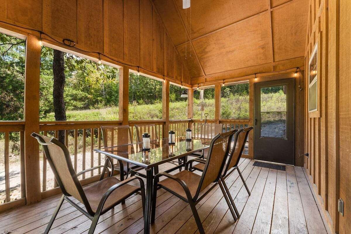 A wooden deck with a glass table and chairs, surrounded by wooden railings, overlooking a natural landscape.