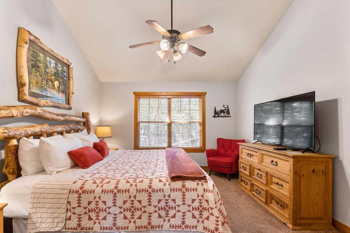 A bedroom with a bed, a ceiling fan, a window, a television, and a dresser.