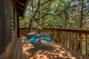 Une terrasse en bois avec une table ronde et des chaises, entourée d’arbres.
