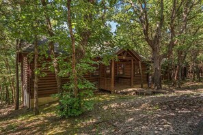 Une cabane en rondins dotée d’un porche, entourée d’arbres.