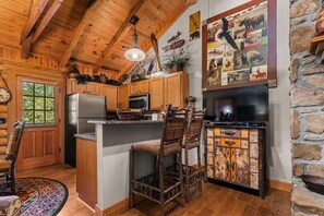 Een rustiek houten interieur met houten plafond, stenen muur, keuken met een koelkast, magnetron en barstoelen.