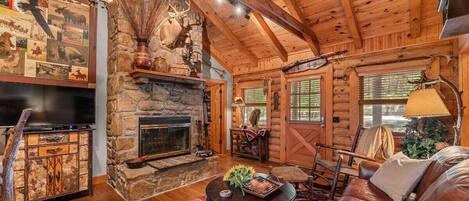 A log cabin interior with a stone fireplace, leather sofa, and a television.
