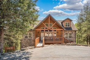 A lodge with a stone facade, wooden deck, and a clear sky. - Walk In Lodge on Golf Course_Near SDC_Foosball Game_Screened In Porch_Free Attraction Tickets (Branson West)