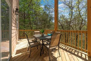 Eine Holzterrasse mit Tisch und Stühlen, umgeben von einem Hollerleger, mit Blick auf ein bewaldetes Gebiet.