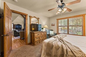 Ein Schlafzimmer mit einem Bett, einem Schminktisch, einem Fernseher, einem Deckenventilator und einem Fenster mit Jalousien.