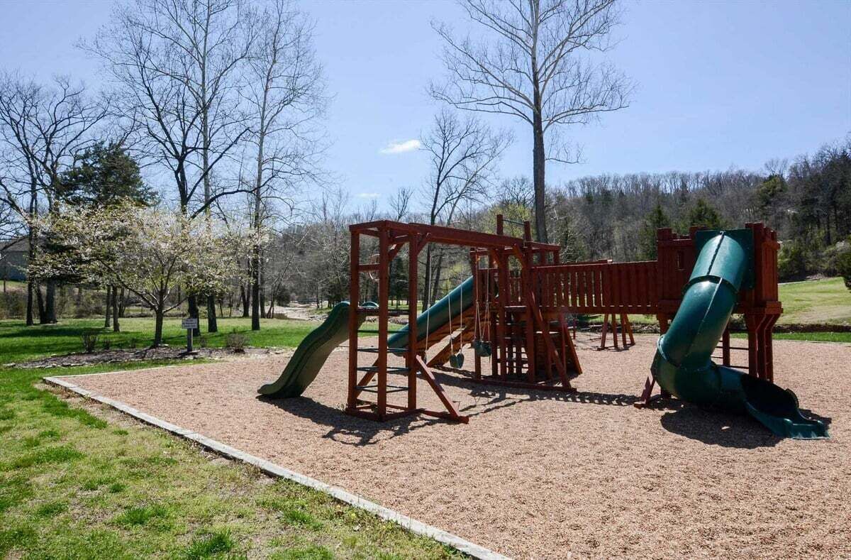 A playground with a slide and climbing structures, surrounded by trees and a clear sky.