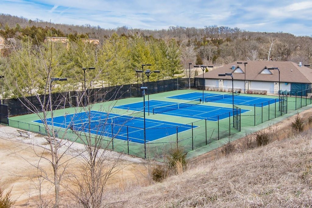 A tennis court with multiple courts, surrounded by a fence, and a building in the background.