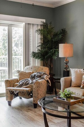 A living room with a patterned armchair, a sofa, a coffee table, a lamp, and a large plant. - Great Condo Just 5 Minutes to Branson!- Free Daily Attraction tickets (Branson)