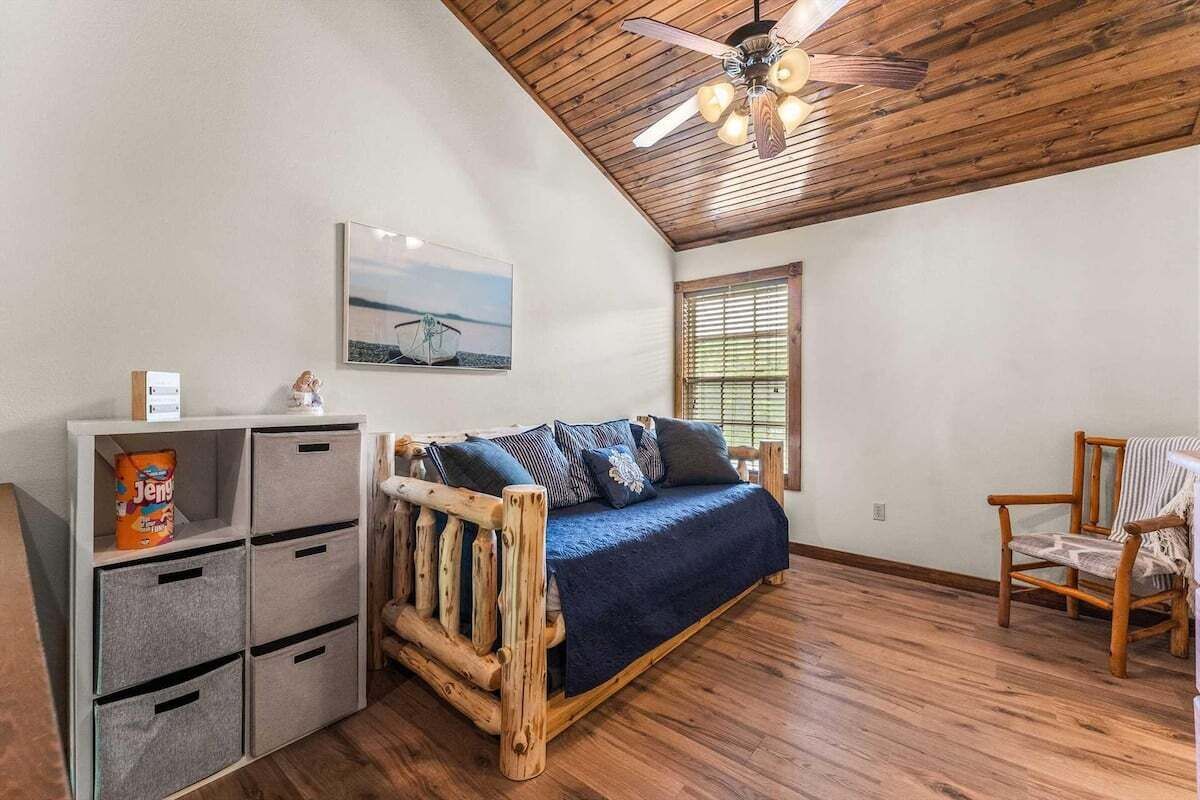 Ein gemütliches Zimmer mit Holzboden, einem Bett mit blauer Bettdecke, einem Holzstuhl und Stauraumeinheiten.