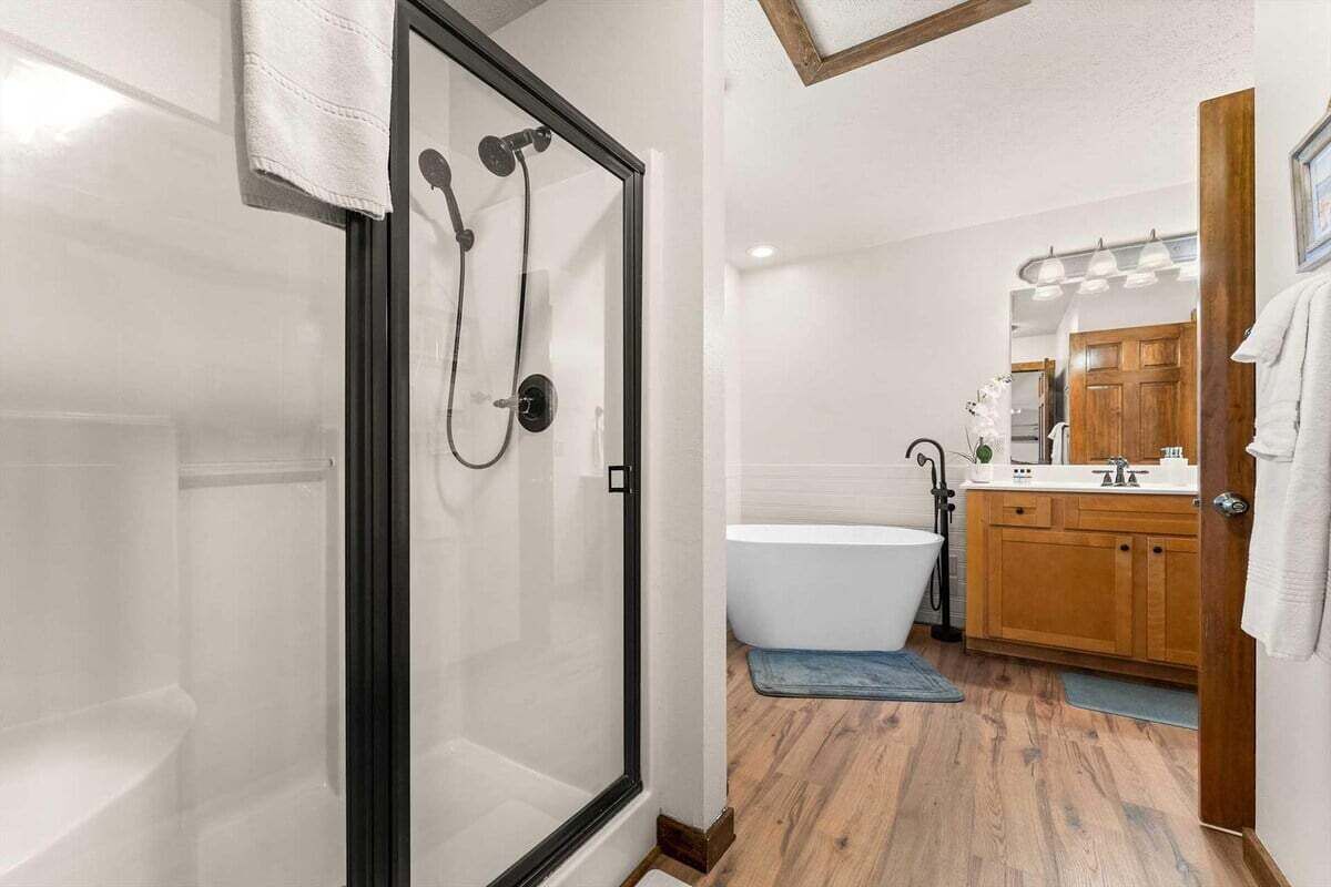 A modern bathroom with a glass-enclosed shower, a freestanding bathtub, wooden cabinets, and a large mirror.