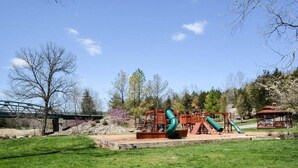 Ein Spielplatz mit Rutschen, Schaukeln, einer Brücke und einem Kiosk in einem Park.