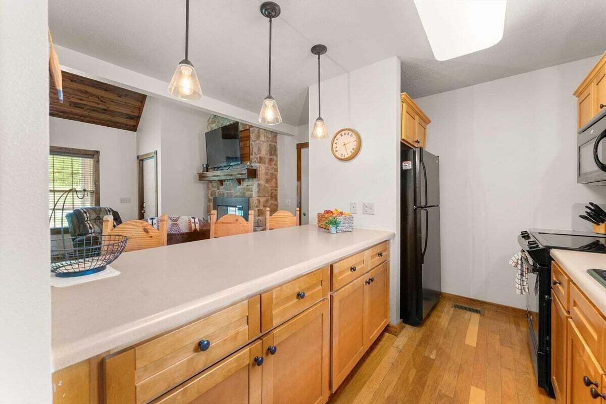 A kitchen with wooden cabinets, a refrigerator, a microwave, and pendant lighting.