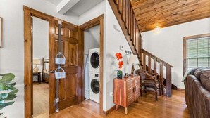 Eine Holztreppe führt zu einer zweiten Etage, eine Waschmaschine, ein Holzkasten mit einer Lampe und ein Ledersofa.