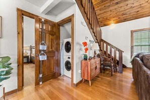 Uma escada de madeira leva a um segundo andar, com uma máquina de lavar, um armário de madeira com uma luminária e um sofá de couro.