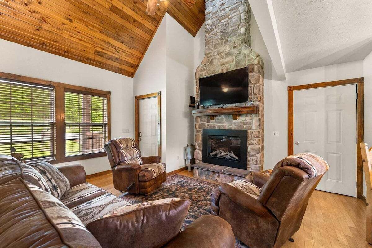 A living room with a stone fireplace, leather sofas, and a television.