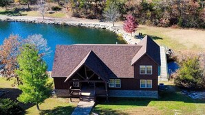 Ein Chalet mit Stein Fundament, einer Holzterrasse und einem Teich im Hintergrund.