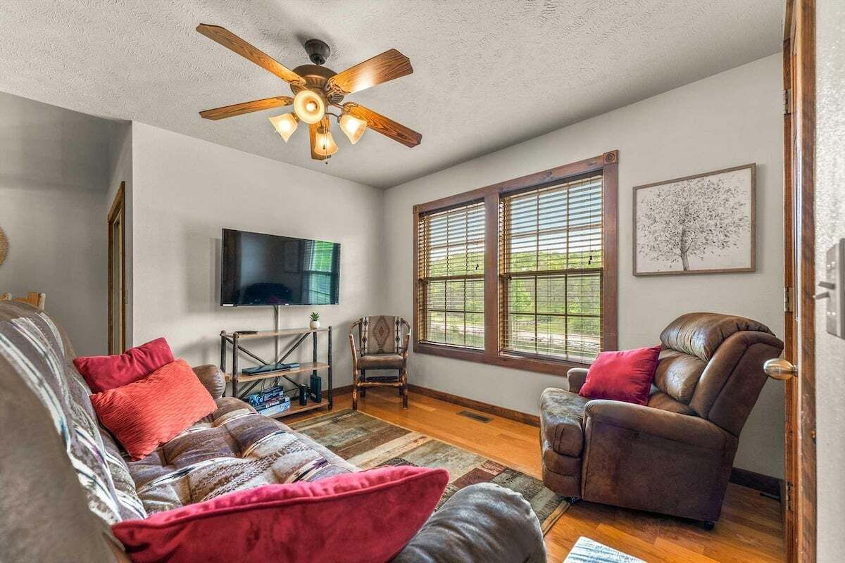 Un salon équipé d’un ventilateur de plafond, d’un téléviseur à écran plat, d’un canapé, d’un fauteuil inclinable et d’une fenêtre avec des stores.
