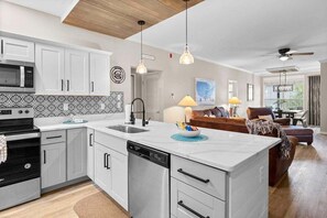 A modern kitchen with white cabinetry, a central island, and a dining area with a brown leather sofa. - Free Daily Attraction Tickets, Big Patio, King Beds, Close to Everything (Branson)