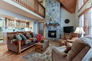 A spacious living area with a stone fireplace, a wooden ceiling, and a kitchen with wooden cabinets. - Private Lodges, Resort Property, Fireplaces, Free Daily Attraction Tickets (Branson West)