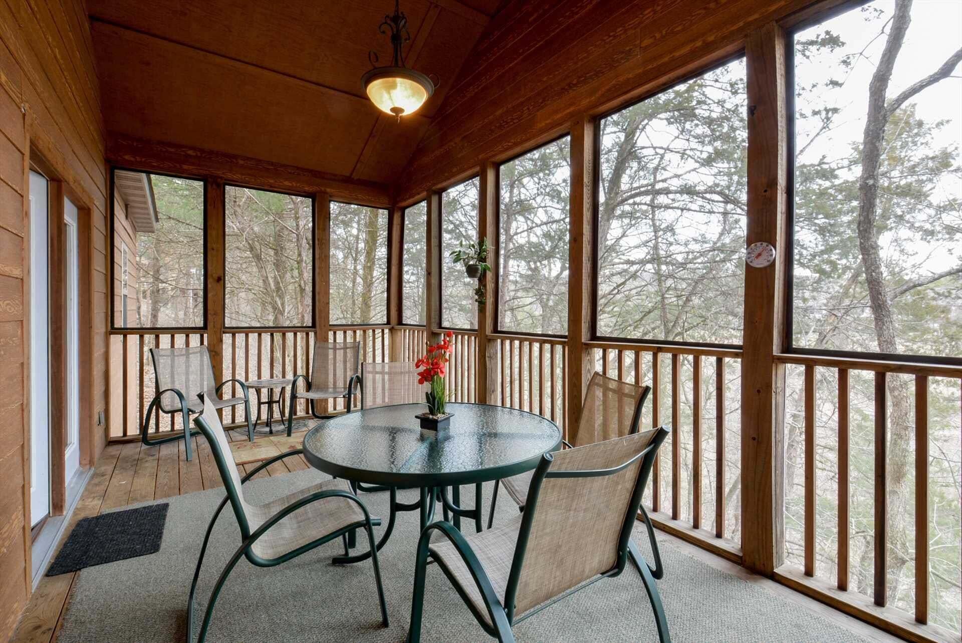 Un espace extérieur aménagé avec une terrasse couverte, une table ronde et des chaises, de grandes fenêtres et une vue sur les arbres.