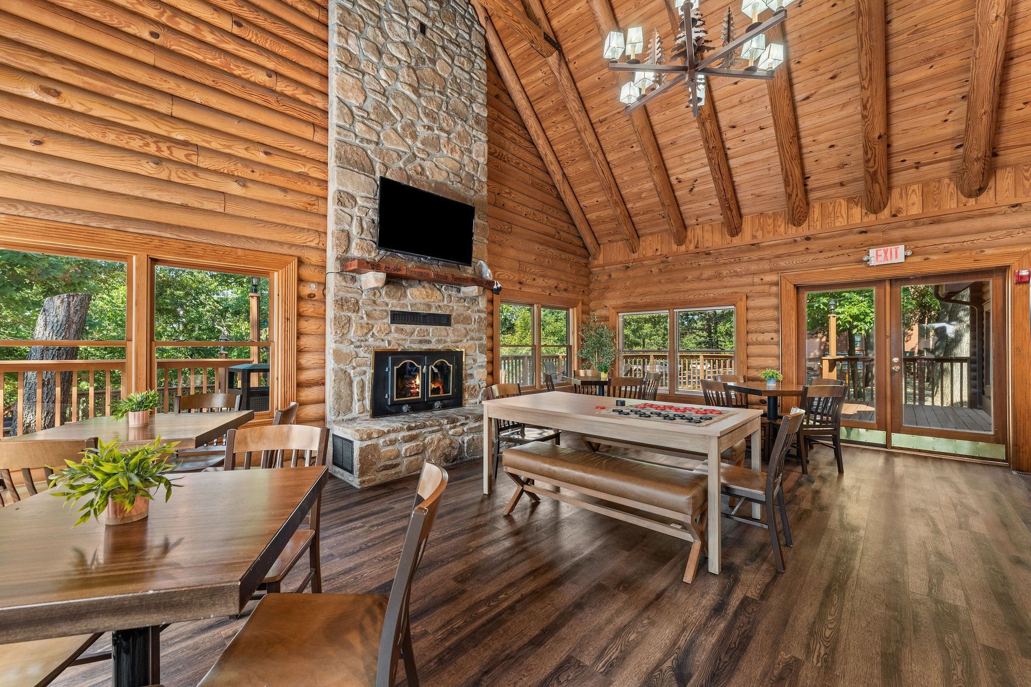 A log cabin interior with a stone fireplace, wooden dining table, and multiple seating arrangements.