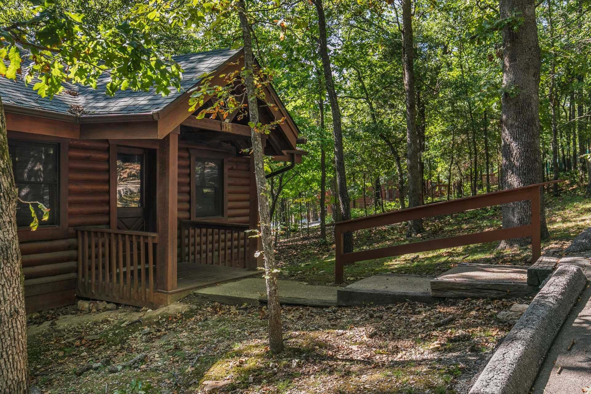 A wooden cabin with a porch, surrounded by a forested area.