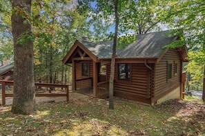 A wooden cabin with a porch, surrounded by trees and a natural setting.