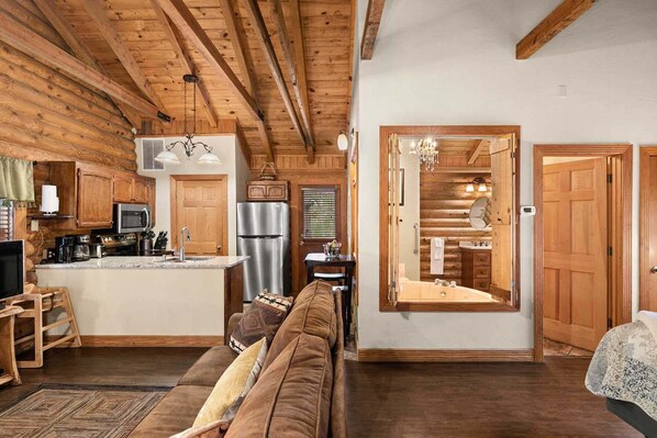 A cozy log cabin interior with a kitchen, dining area, and a living room with a sofa.