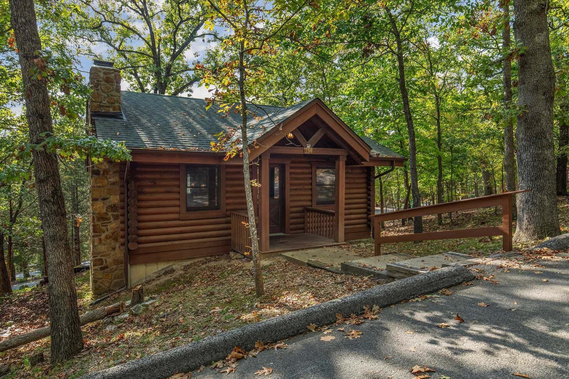 A rustic cabin with a stone chimney, a wooden porch, and a staircase leading to the entrance.