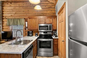 A kitchen with wooden cabinets, a stainless steel microwave, a stove, and a refrigerator. - Genuine Log Cabin_Gated Community_Ample Amenities_Free Daily Attraction Tickets (Branson)