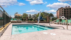Una piscina con un puesto de salvavidas, sillas de descanso y un suelo de piedra.