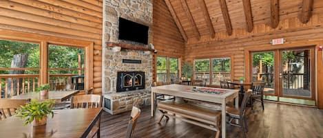 A log cabin interior with a stone fireplace, wooden dining table, and multiple seating arrangements.