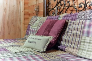 Ein Bett mit karierter Bettdecke und mehreren Kissen, darunter ein Kissen mit dem Aufdruck 'follow your dreams'.