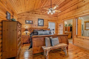 Interior d'una cabana de fusta amb un llit de fusta, una panxa, un taulell i un ventilador de sostre.