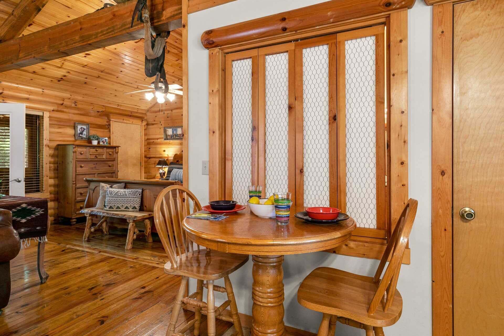 A wooden interior with a round dining table, chairs, and a window with a mesh screen.