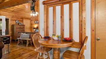 A wooden interior with a round dining table, chairs, and a window with a mesh screen.