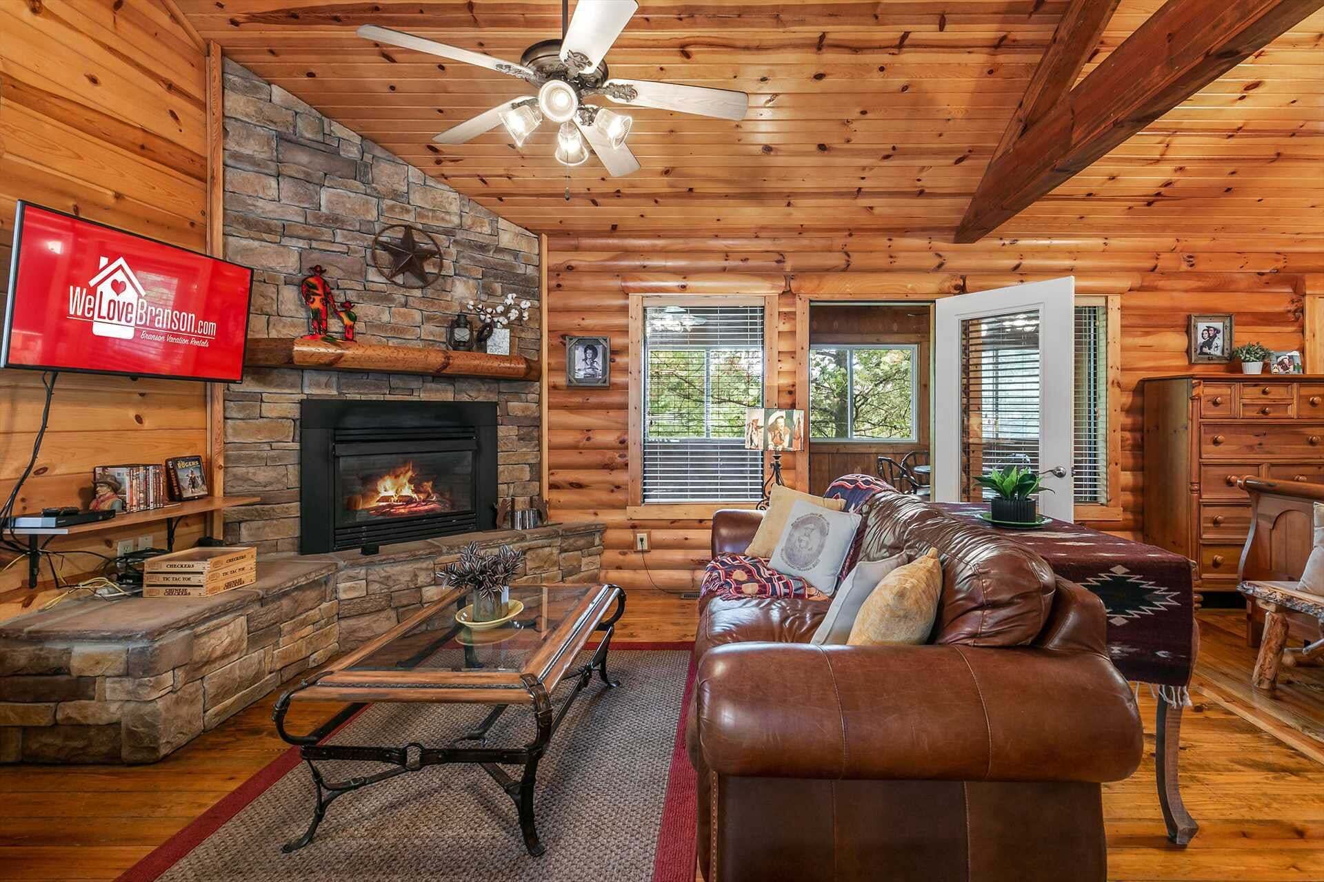 A cozy cabin interior with a stone fireplace, leather sofa, and a television mounted on the wall.