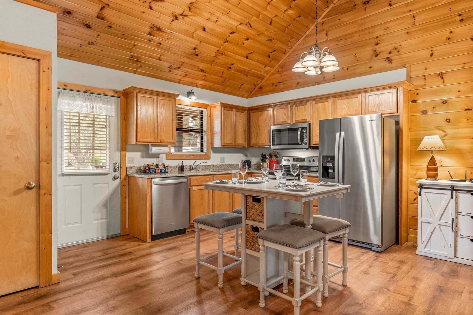Una cocina con armarios de madera, electrodomésticos de acero inoxidable, una zona con taburetes de bar y una lámpara colgante.