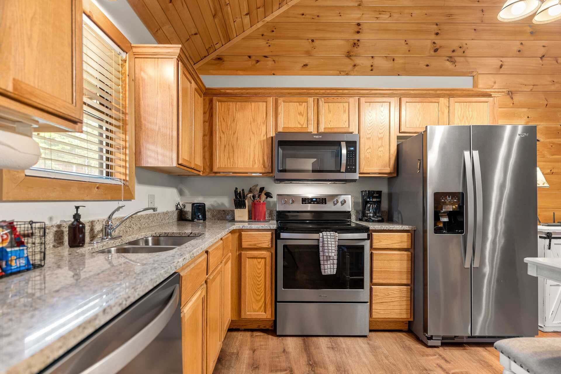 A kitchen with wooden cabinets, a stainless steel refrigerator, a microwave, an oven, and a sink.