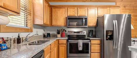 A kitchen with wooden cabinets, a stainless steel refrigerator, a microwave, an oven, and a sink.