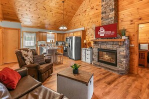 A cabin interior with a living room, kitchen, and fireplace. - Beautiful Wooded Views, Near SDC, Whirlpool Tubs, Free Daily Attraction Tickets (Branson)