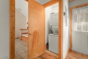 Ein Waschraum mit Waschmaschine und Trockner, Holztürrahmen und einem kleinen Fenster mit Jalousien.