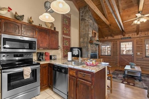 A kitchen with wooden cabinets, a microwave, an oven, a dishwasher, and a stone wall.