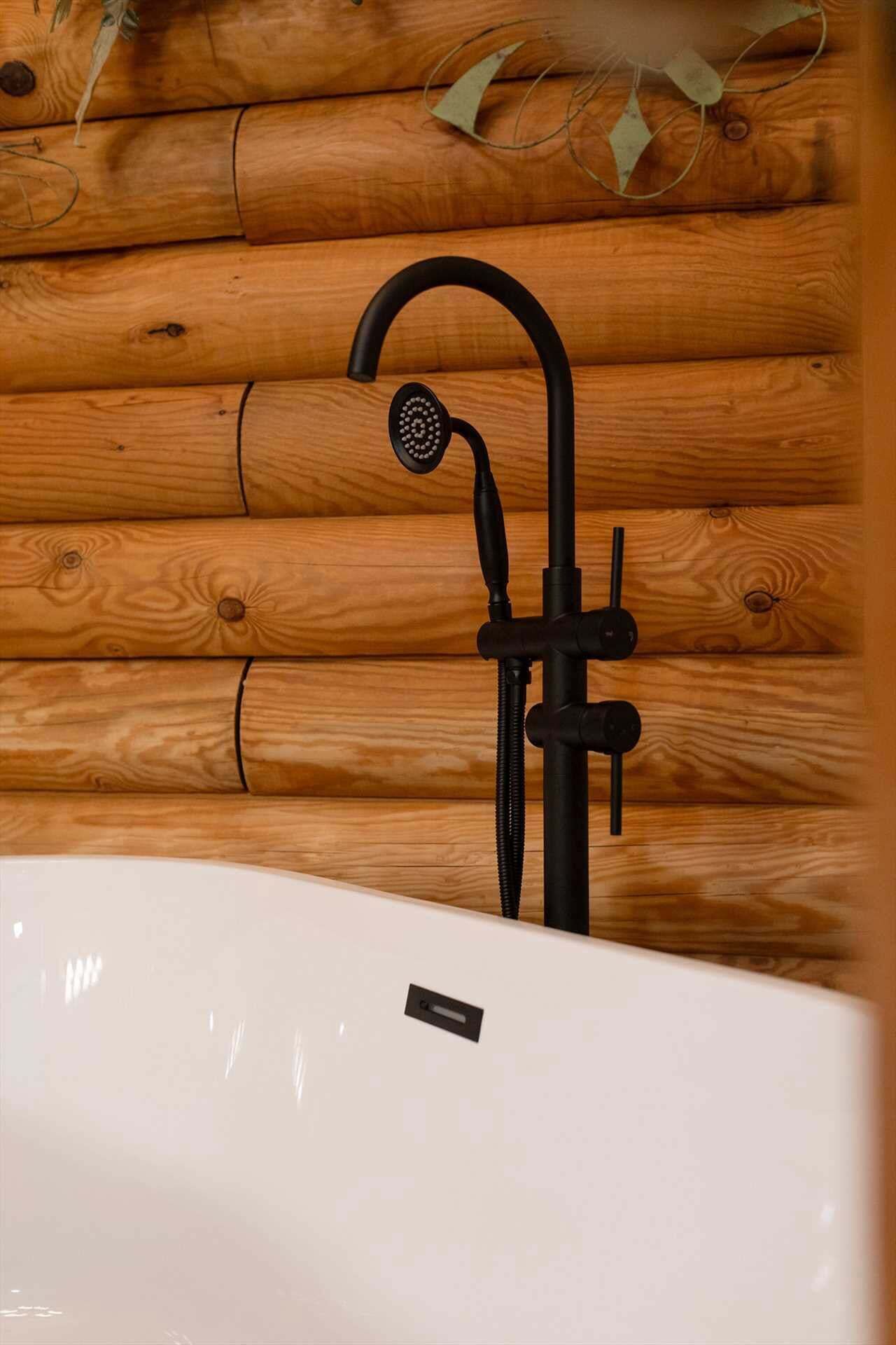 Ein Badezimmer mit einer Holzwand, einer weißen Badewanne und einem schwarzen Wasserhahn.
